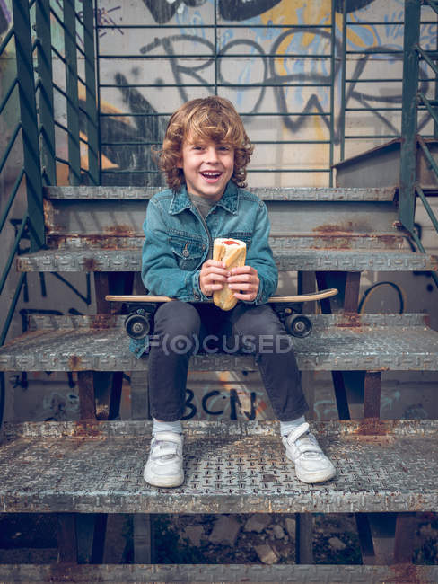 Niño con monopatín sentado en las escaleras - foto de stock
