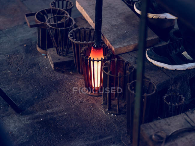Pipe with glass and feet of unrecognizable person on glassblowing factory. — Stock Photo
