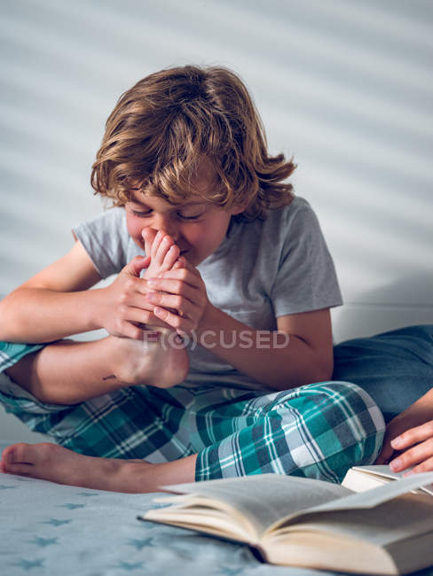 Boy smelling foot on bed — Stock Photo