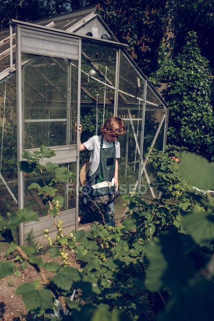 Boy standing in font of greenhouse — Stock Photo
