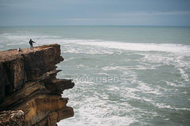 Мужчина рыбачит на большой скале — стоковое фото