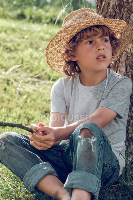 Босоногий мальчик сидит под деревом — стоковое фото