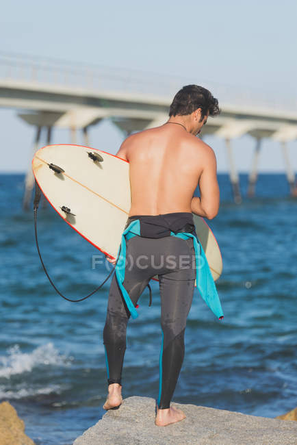 Uomo con tavola da surf in piedi sulla costa — Foto stock