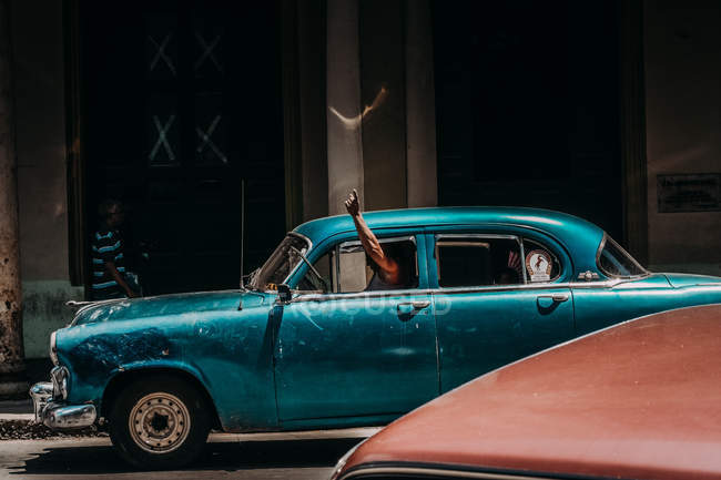 LA HABANA, CUBA - 1 DE MAYO DE 2018: Vista lateral del conductor en automóvil de época conduciendo por la carretera de la ciudad en Cuba haciendo gestos a la luz del sol . - foto de stock