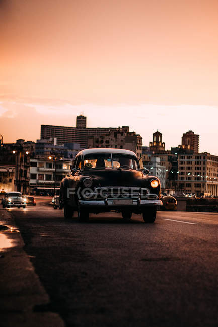 Vintage car driving down road in sunset — Stock Photo