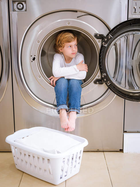 Bonito elementar idade menino sentado dentro de máquina de lavar roupa — Fotografia de Stock