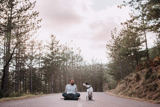 Homem com cão sentado na estrada — Fotografia de Stock