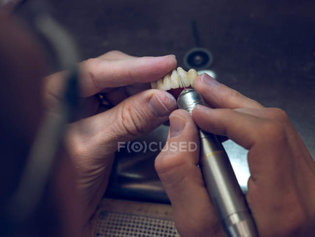 Técnico tallando dientes en prótesis dentales - foto de stock