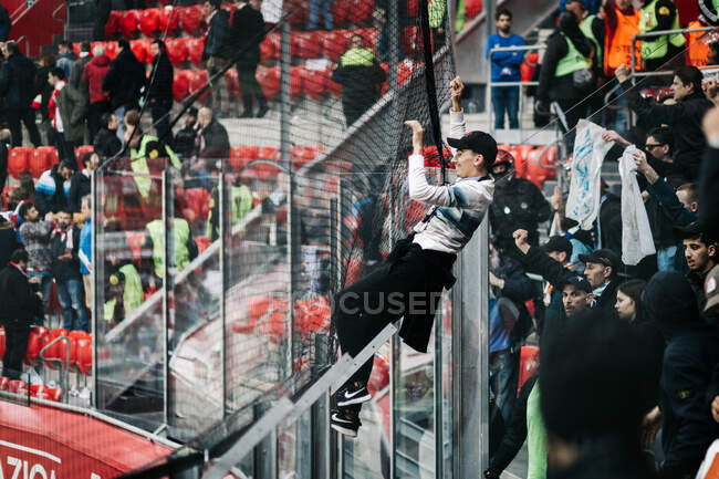 Fan climbing on the net in stadium — Stock Photo