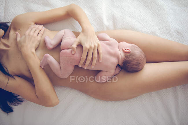 De dessus la culture femme nue couché avec bébé enfant sur le lit. — Photo de stock
