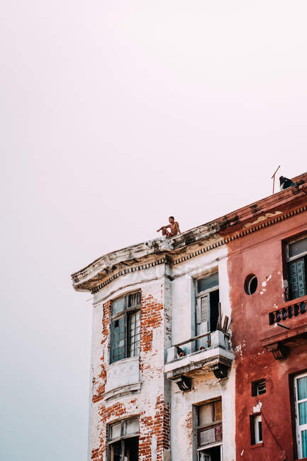 Von unten erschossen erschossener Mann auf dem Dach eines schönen und schäbigen Hauses unter sauberem Himmel, Kuba. — Stockfoto