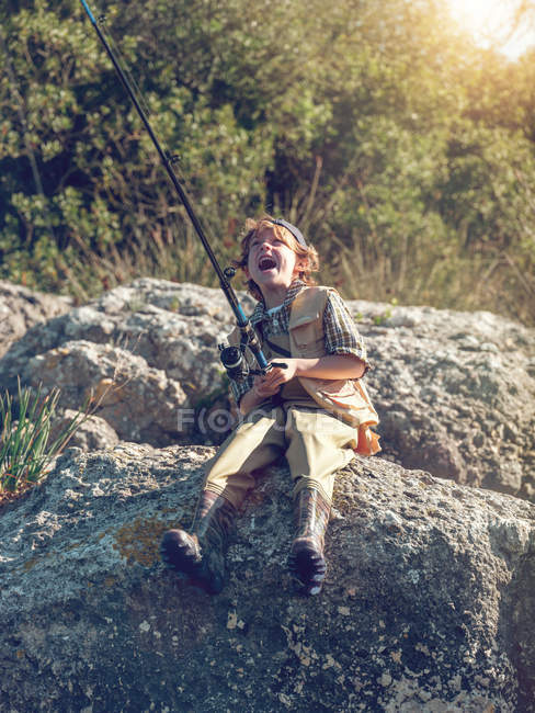 Мальчик со стержнем сидит на камне — стоковое фото