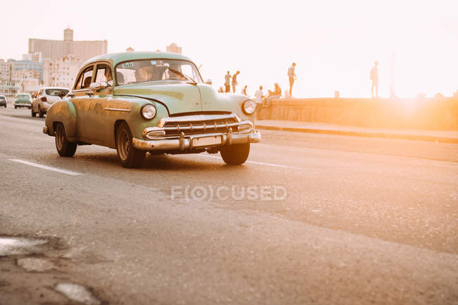 Coche de época conduciendo por carretera al atardecer, Cuba - foto de stock