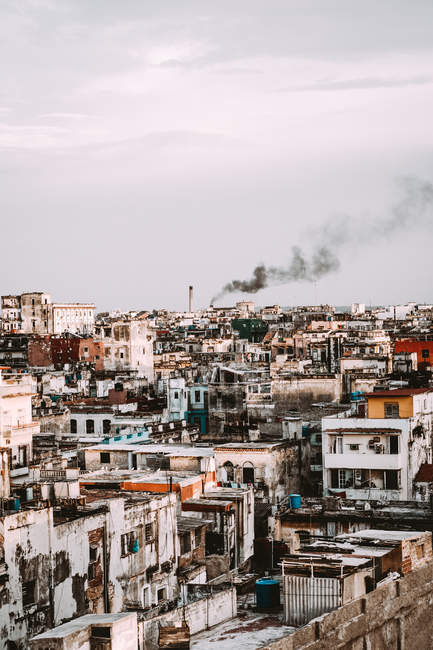 Old shabby city buildings and houses with black smoke on background, Cuba — Stock Photo