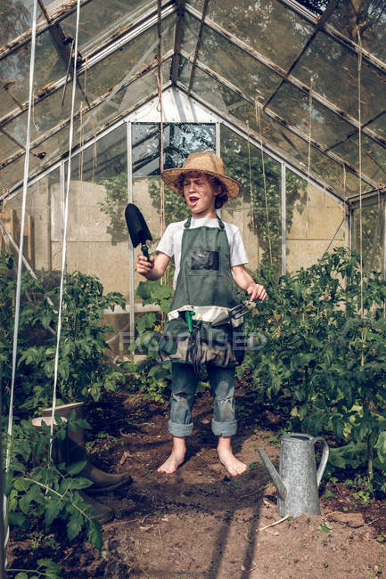 Boy standing in greenhouse with shovel — Stock Photo