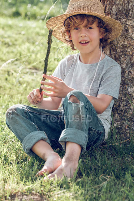 Little boy in hat sitting under tree — Stock Photo