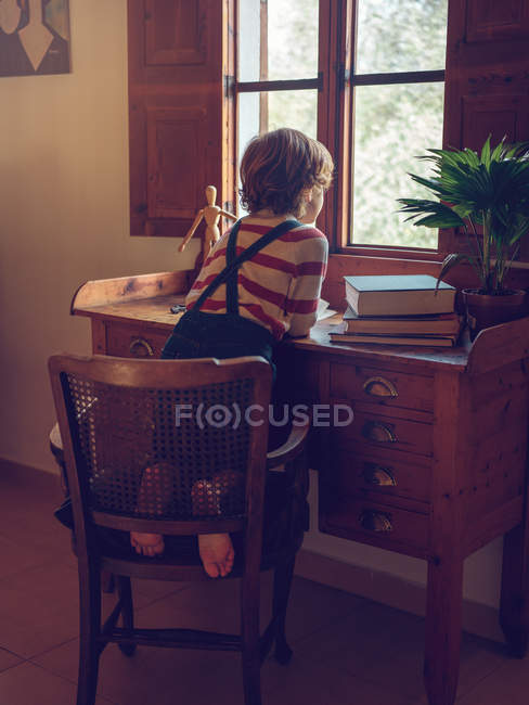 Niño sentado en la silla en el escritorio - foto de stock