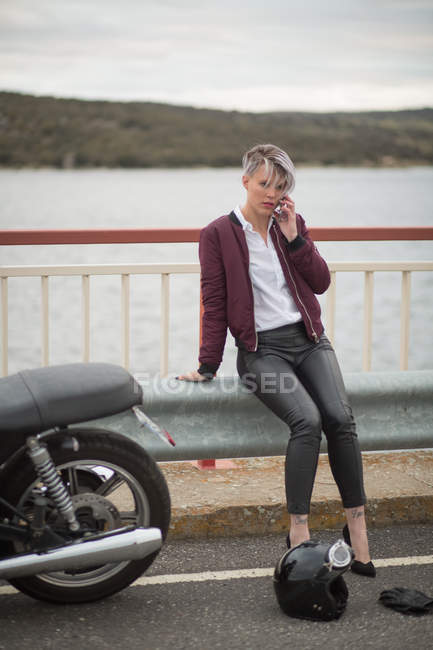 Mulher falando no smartphone ao lado de moto — Fotografia de Stock
