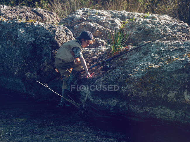 Мальчик карабкается на скалу с удочкой — стоковое фото