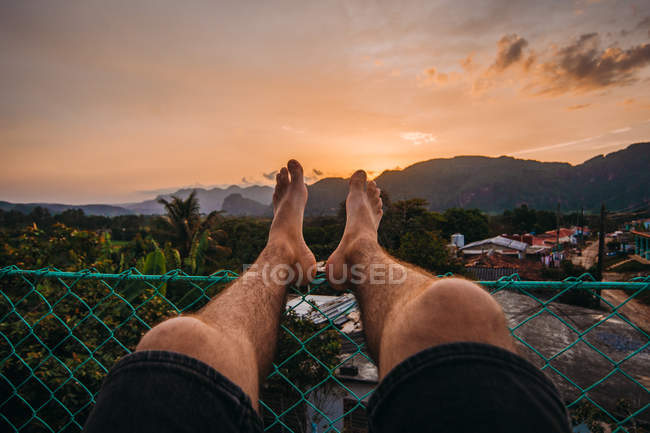 Gambe maschili appoggiate sulla recinzione del cortile con splendida vista sulle montagne del tramonto nei tropici di Cuba — Foto stock