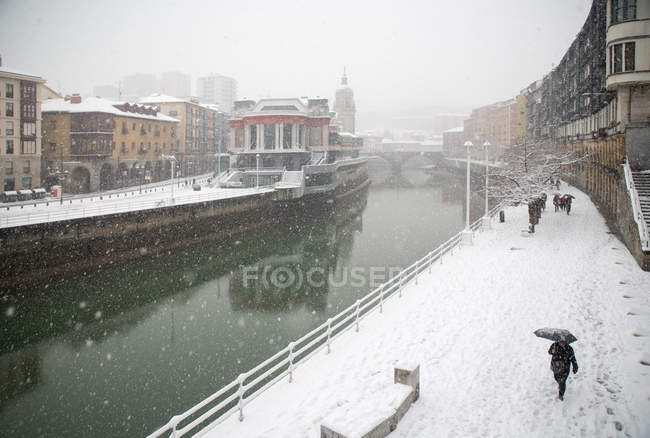 Canal fluvial y calle cubierta de nieve en Bilbao, España . - foto de stock