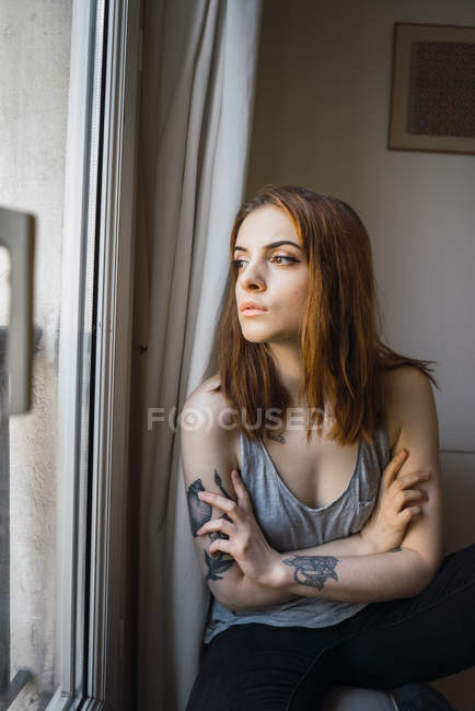 Mujer tatuada sentada en la ventana - foto de stock