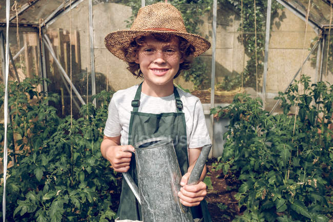 Niño sosteniendo regadera en invernadero - foto de stock