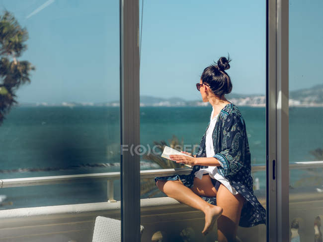 Junge Frau entspannt mit Buch auf Balkon am Meer. — Stockfoto