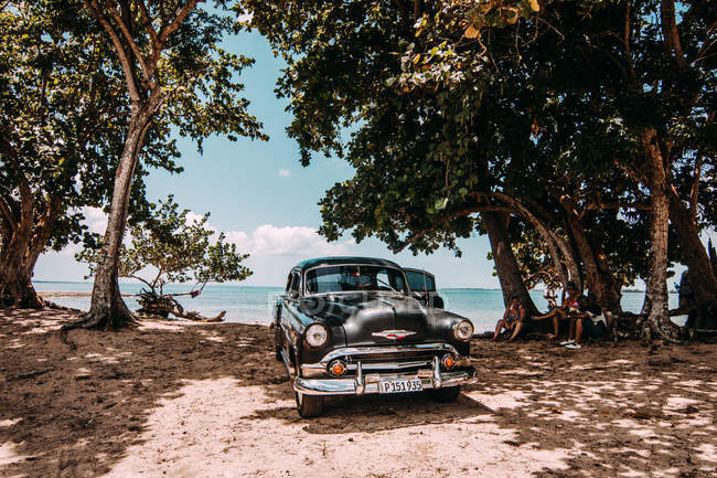 LA HABANA, CUBA - MAY 1, 2018: black retro car parked on sandy tropical coastline of Cuba in sunlight — Stock Photo
