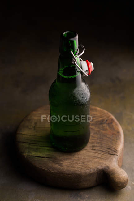 Garrafa de cerveja na placa de madeira no fundo escuro — Fotografia de Stock