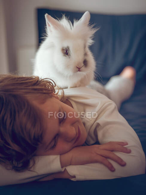 Menino deitado e dormindo com coelho branco em uma cama. — Fotografia de Stock