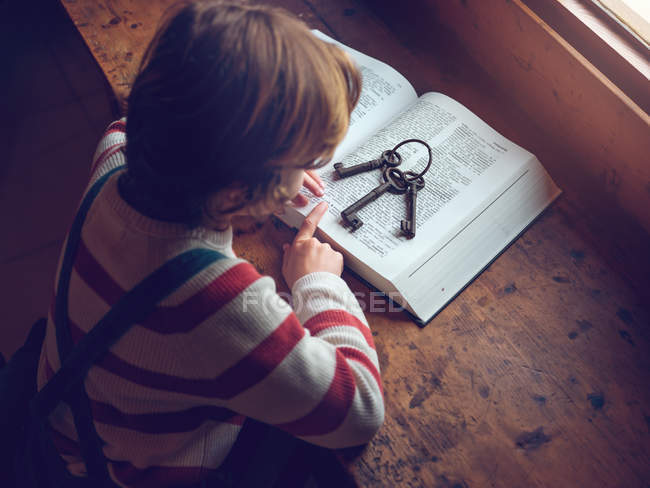 Niño sentado con llaves en el libro - foto de stock