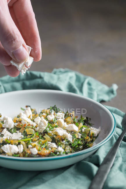 Human hand putting feta in stuffing for traditional spanakopita spinach pie — Stock Photo