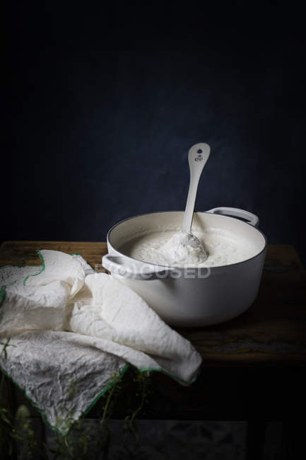 Pentola bianca con fiocchi di latte incompleti sul tavolo . — Foto stock