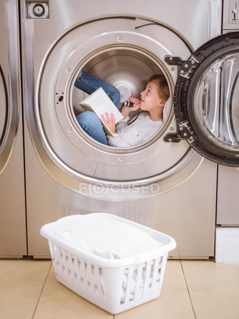 Ragazzo dell'età elementare con torcia elettrica sdraiato dentro lavatrice con libro . — Foto stock