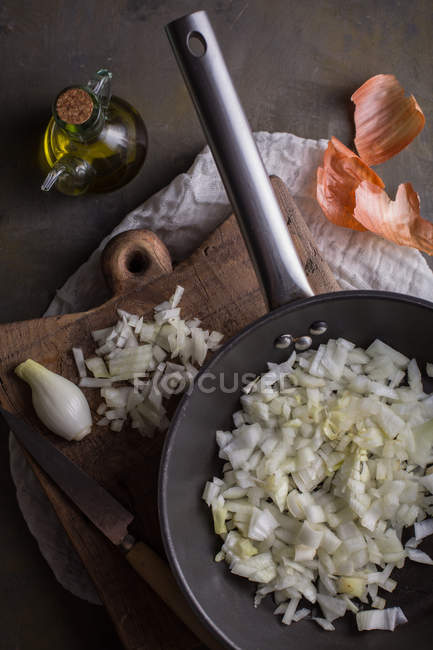Chopped fresh onion in frying pan and on wooden chopping board — Stock Photo