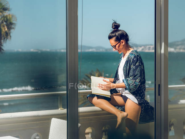 Giovane donna lettura libro al balcone sulla riva del mare
. — Foto stock