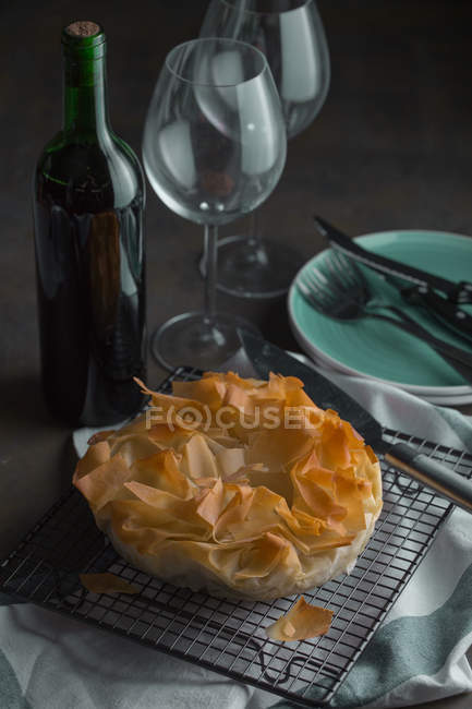 Traditional greek spinach pie spanakopita on baking rack and wine bottle — Stock Photo