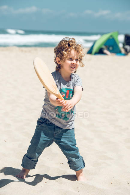 Menino com raquete de madeira na praia — Fotografia de Stock