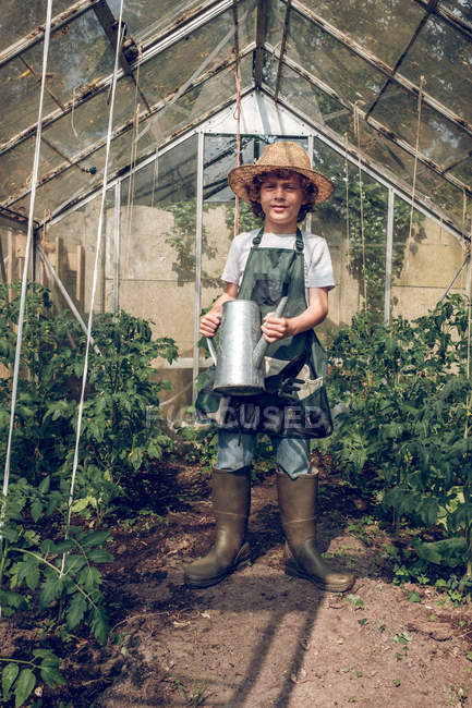 Boy standing with watering can in greenhouse — Stock Photo