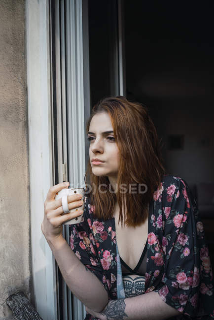 Жінка з чашкою спирається на вікно — стокове фото