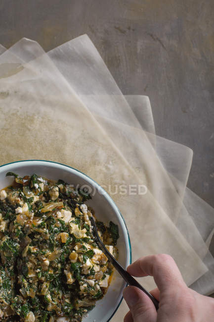 Human hand stirring stuffing for traditional spanakopita spinach pie in bowl — Stock Photo