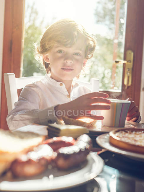 Маленький хлопчик з чашкою сидить за столом — стокове фото