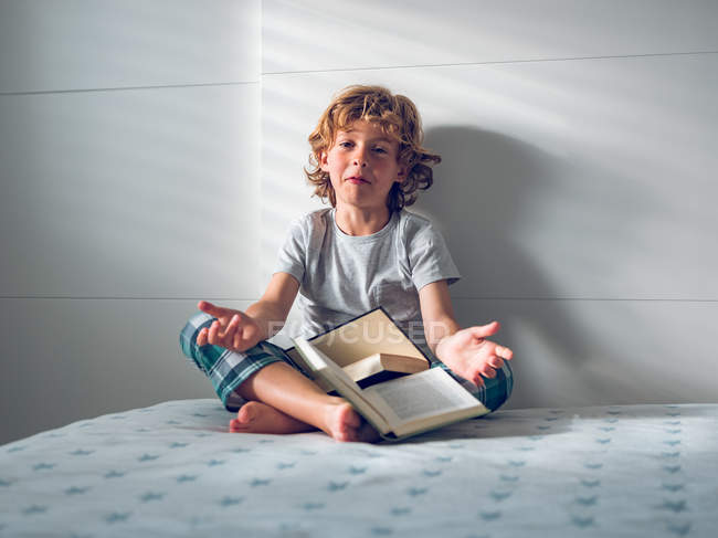 Niño en pijama sentado con libros - foto de stock