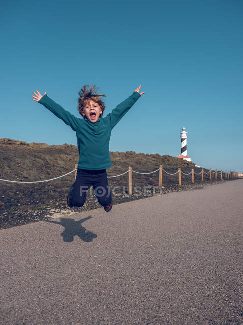 Хлопчик стрибає перед маяком — стокове фото