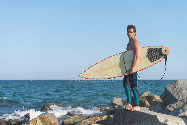 Человек с доской для серфинга стоит на берегу — стоковое фото