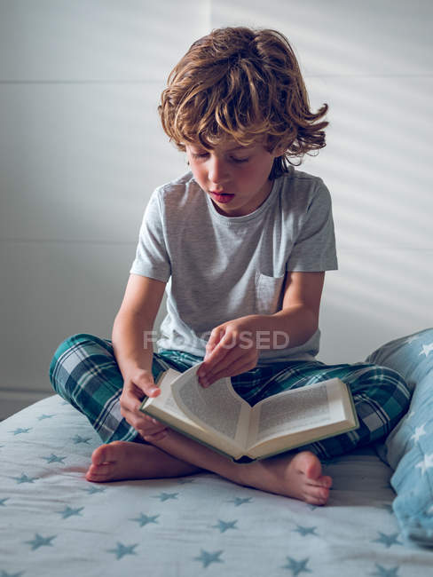 Мальчик читает книгу на кровати — стоковое фото