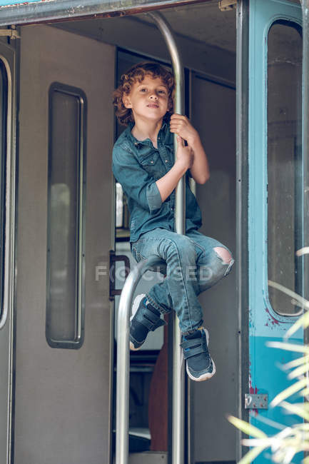 Niño sentado en barandilla en vagón abandonado - foto de stock