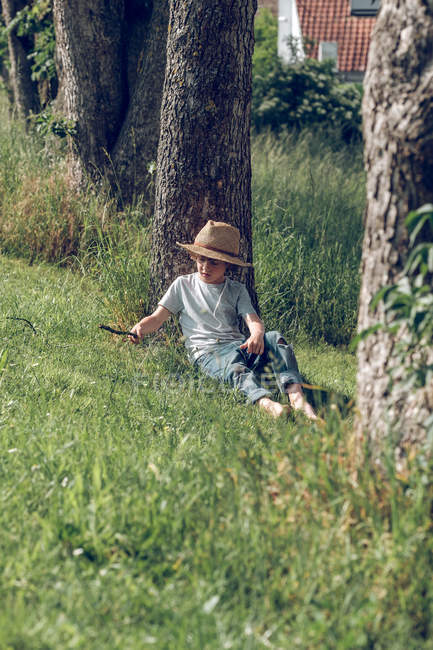 Маленький хлопчик у капелюсі сидить під деревом — стокове фото