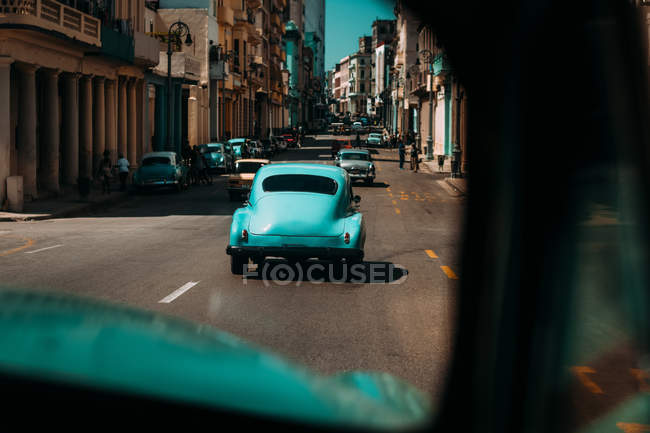 Старомодные автомобили на городской дороге с потрепанными зданиями, Куба — стоковое фото